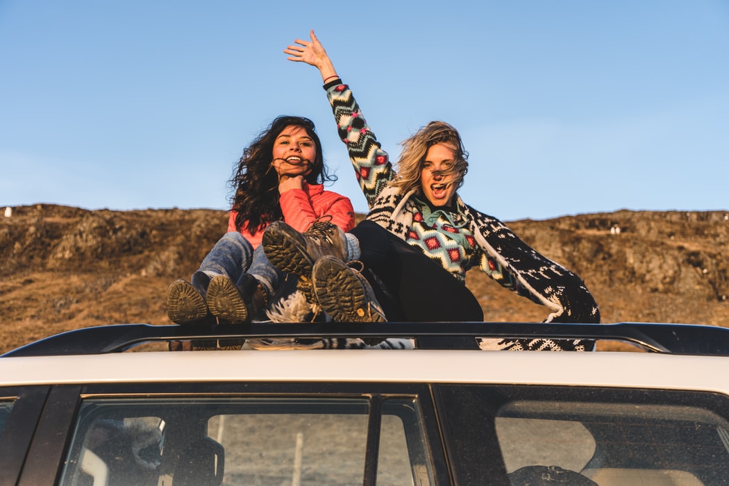 two woman sitting on top of car